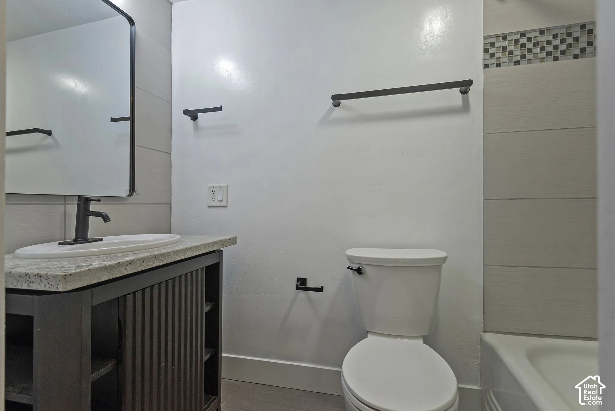 Bathroom featuring a vanity with a stone-top surface and vessel sink, matte black hardware, rectangular mirror with a metal frame, and tile surround in the tub area
