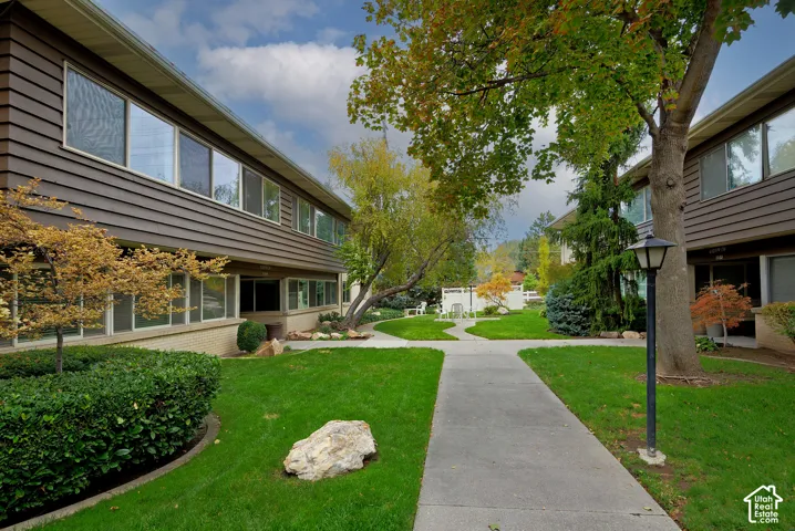 Exterior featuring brown horizontal siding, concrete walkways, manicured lawn, mature landscaping, and an integrated post light