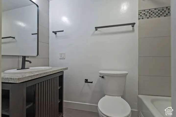 Bathroom featuring a vanity with a stone-top surface and vessel sink, matte black hardware, rectangular mirror with a metal frame, and tile surround in the tub area