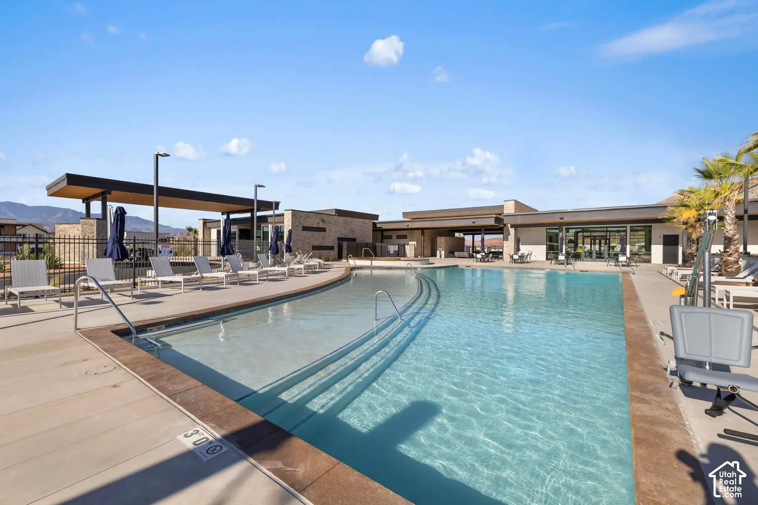 Swimming pool featuring a beach entry, concrete decking, stone-clad perimeter walls, and an integrated covered structure
