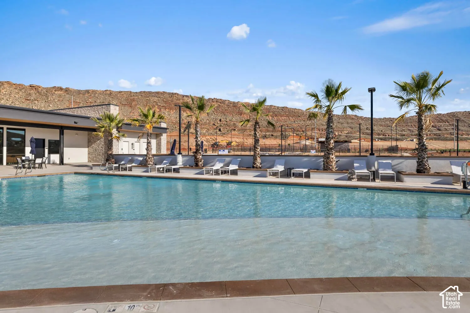 Swimming pool with a zero-entry design, concrete decking, stone-accented architecture, and palm tree landscaping
