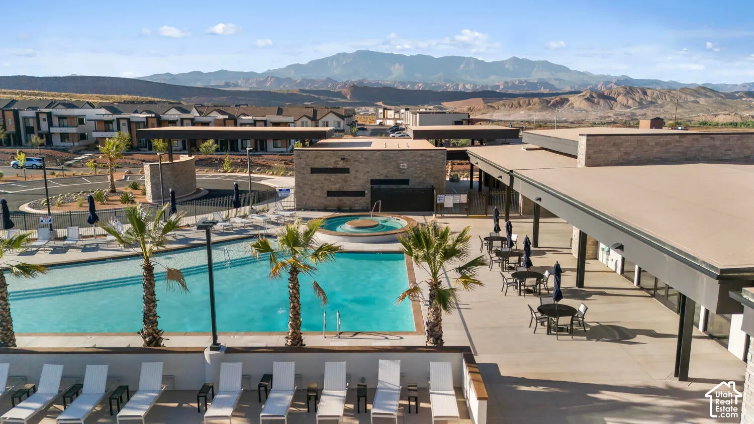 Community pool with integrated hot tub, expansive concrete patio, and stone masonry architecture set against a prominent mountain backdrop