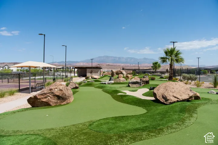 Putting green featuring artificial turf, decorative boulders, and pole-mounted lighting, accompanied by a tennis court and shade structure