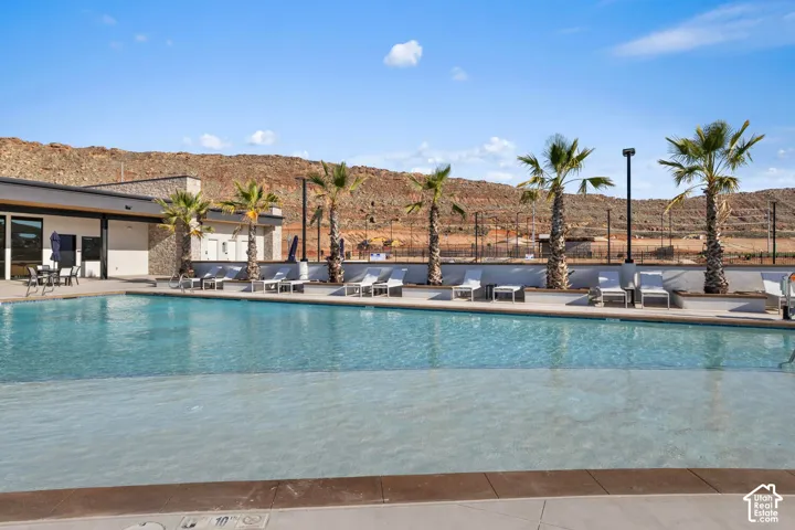 Swimming pool with a zero-entry design, concrete decking, stone-accented architecture, and palm tree landscaping