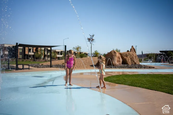 Community splash pad featuring integrated water jets, a concrete basin, manicured lawn areas, and decorative boulder hardscaping