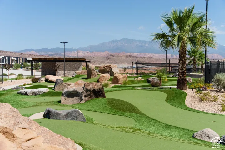 Putting green featuring synthetic turf, decorative boulder accents, and palm tree landscaping set against a mountain backdrop
