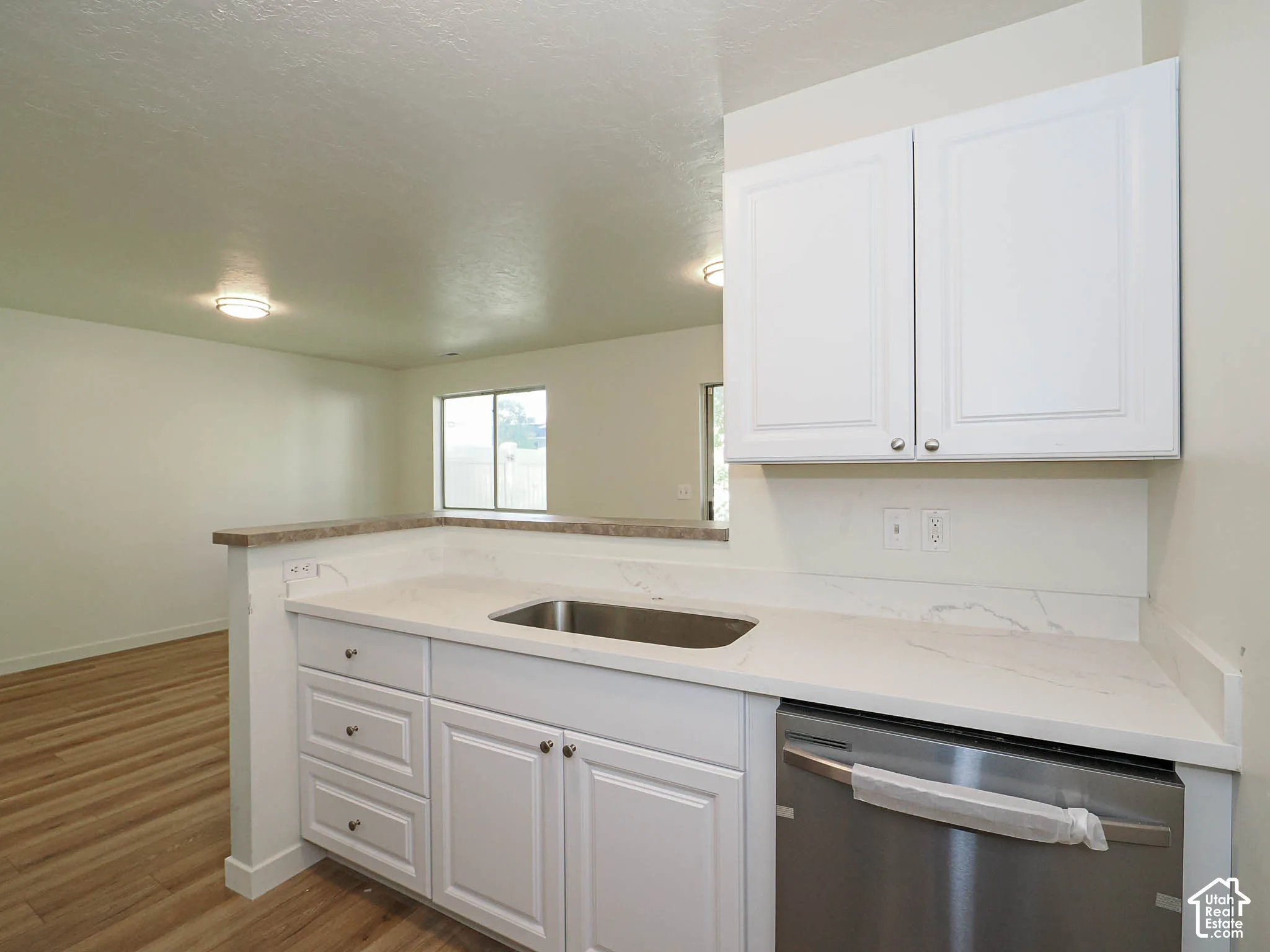 Kitchen featuring white shaker-style cabinetry, white countertops with grey veining, stainless steel undermount sink, stainless steel dishwasher, and wood-finish flooring