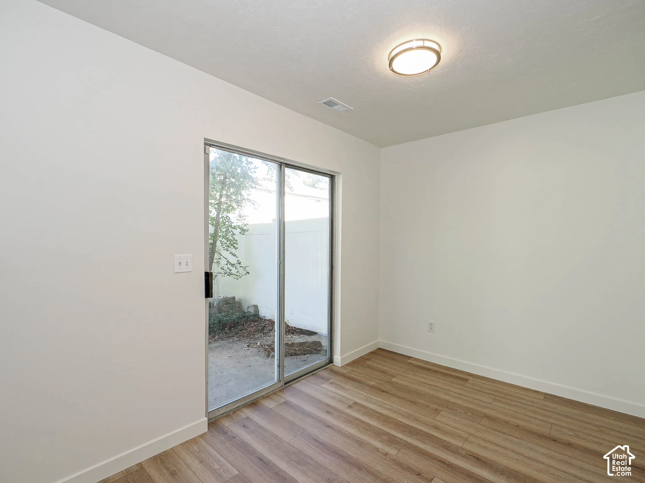 Interior space featuring wood-finish flooring, neutral wall tones, flush-mount ceiling lighting, and a sliding glass door providing exterior access