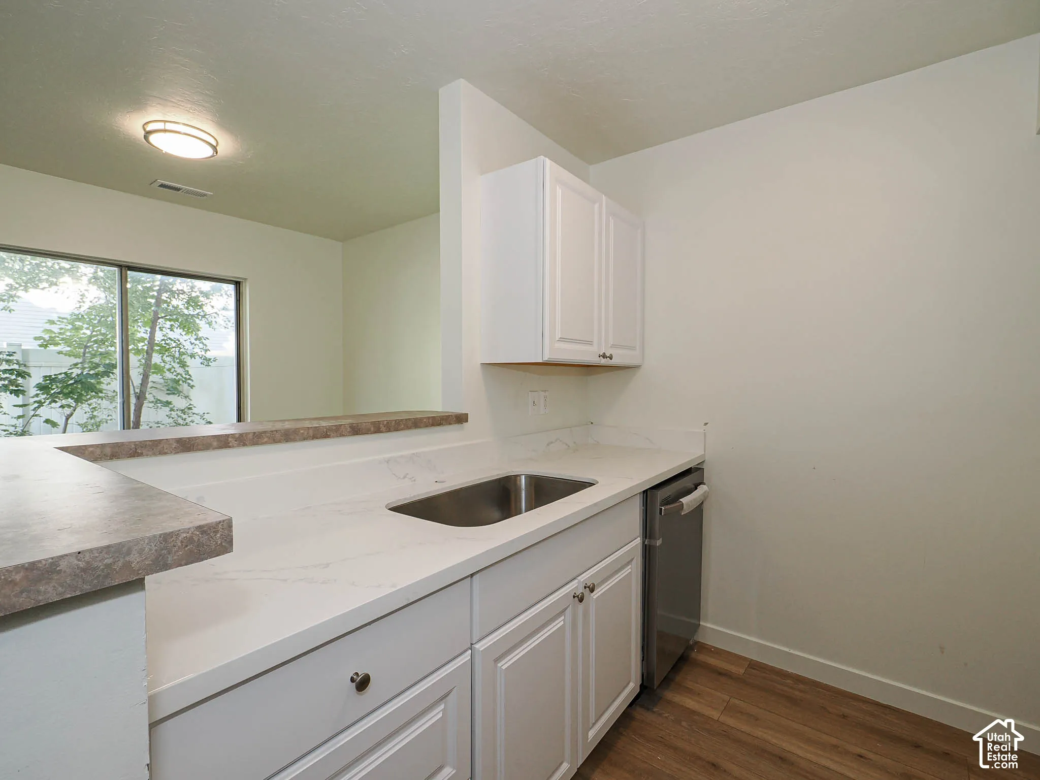 Kitchen featuring white shaker-style cabinetry, quartz countertops, an undermount stainless steel sink, a stainless steel dishwasher, and wood-finish flooring
