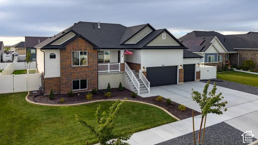 Two-story residence featuring a mixed brick and horizontal siding exterior, attached three-car garage, concrete driveway, and front entryway with elevated staircase and white railing