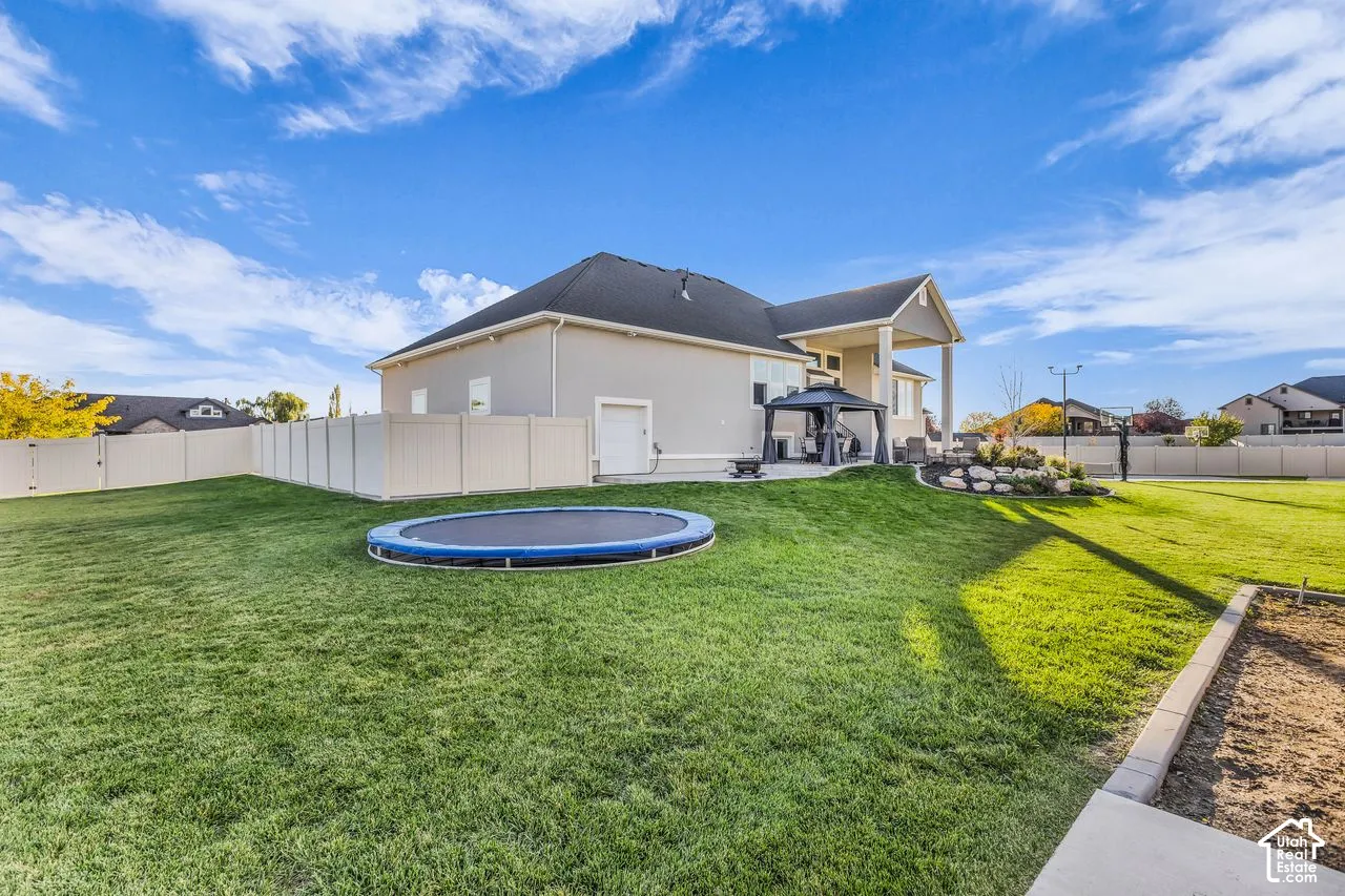 Expansive backyard featuring a fenced perimeter, stone-bordered landscaping, and a covered concrete patio
