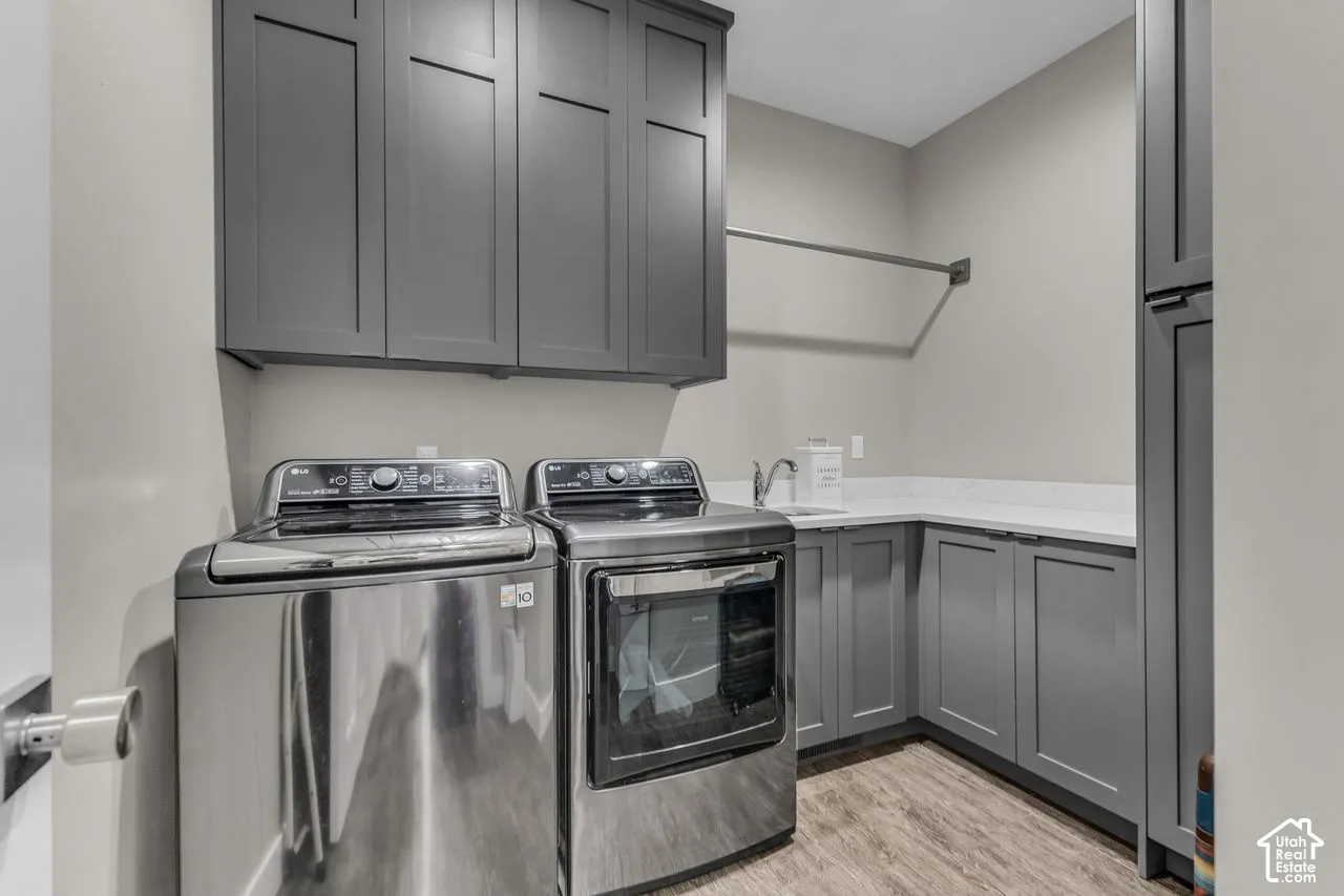 Laundry space featuring charcoal shaker-style cabinetry, a stone-composite countertop, an integrated sink with a chrome faucet, and wood-finish flooring