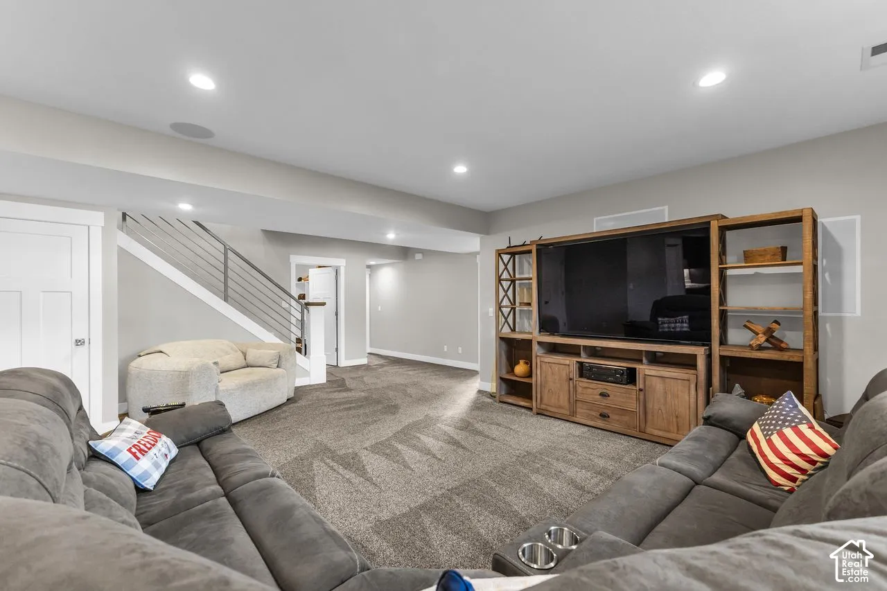 Open-concept room featuring recessed lighting, a large built-in wood media console, carpeted flooring, and a staircase with metal horizontal railings