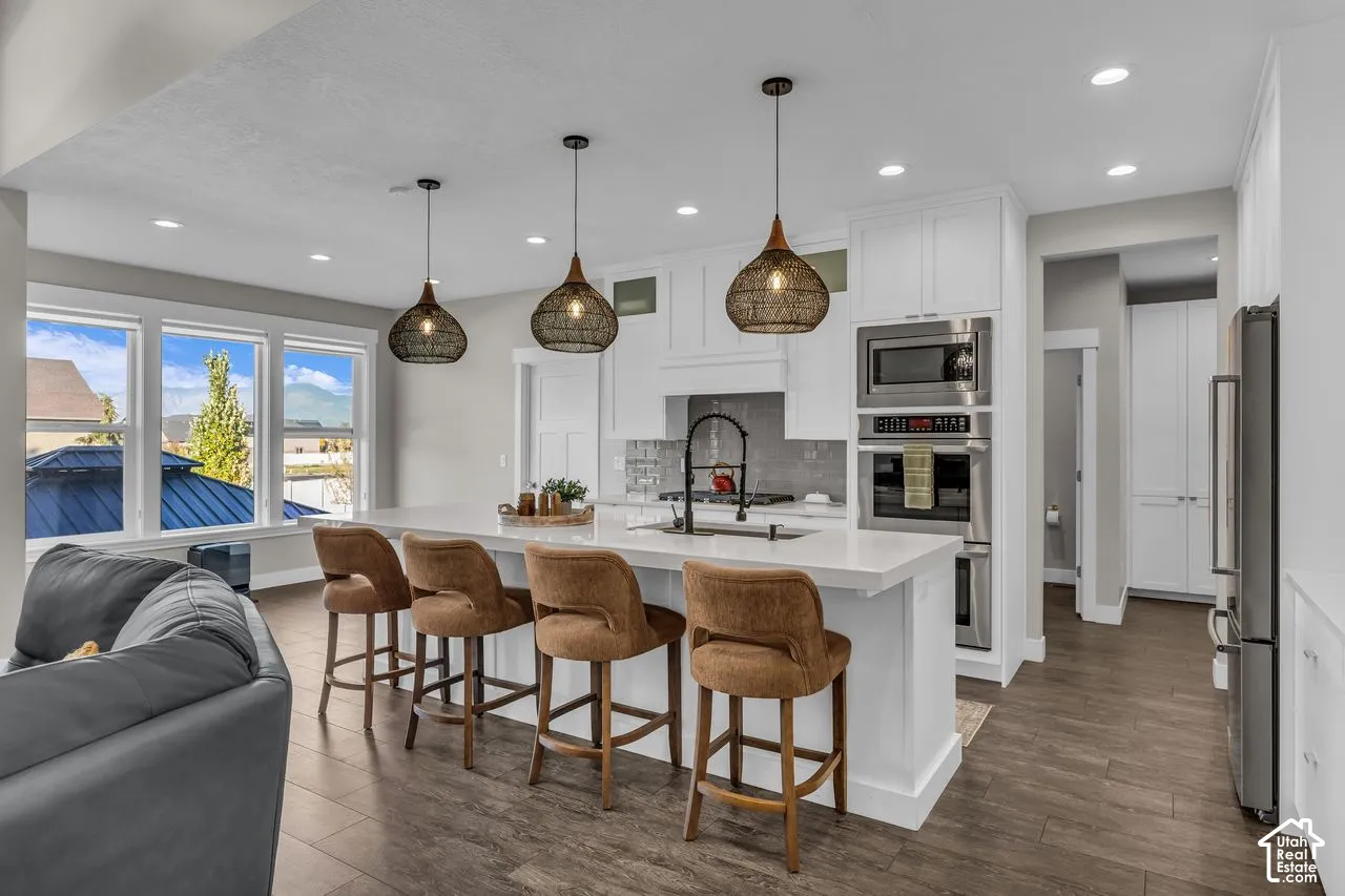 Kitchen featuring white cabinetry, an expansive quartz-topped island, built-in stainless steel double ovens, wood-finish flooring, and three oversized woven pendant lights