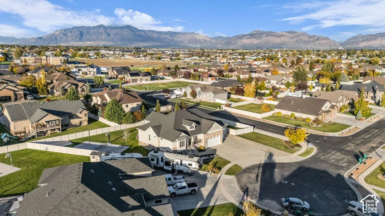Aerial perspective featuring a multi-gabled residence with stone and siding exterior, expansive concrete driveway, multi-car garage, and prominent mountain backdrop