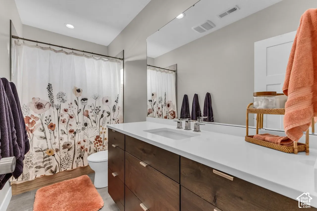 Dark wood-finish cabinetry featuring horizontal pulls, white solid-surface countertop, undermount sink with widespread faucet, wall-to-wall mirror, and recessed lighting