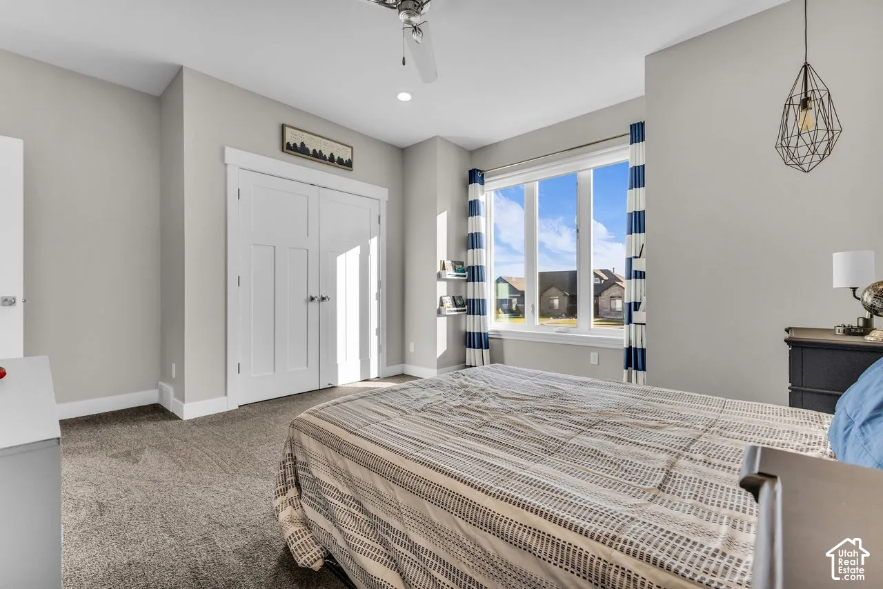 Room featuring carpeted flooring, a large picture window, double-panel closet doors, a geometric pendant light, and a ceiling fan