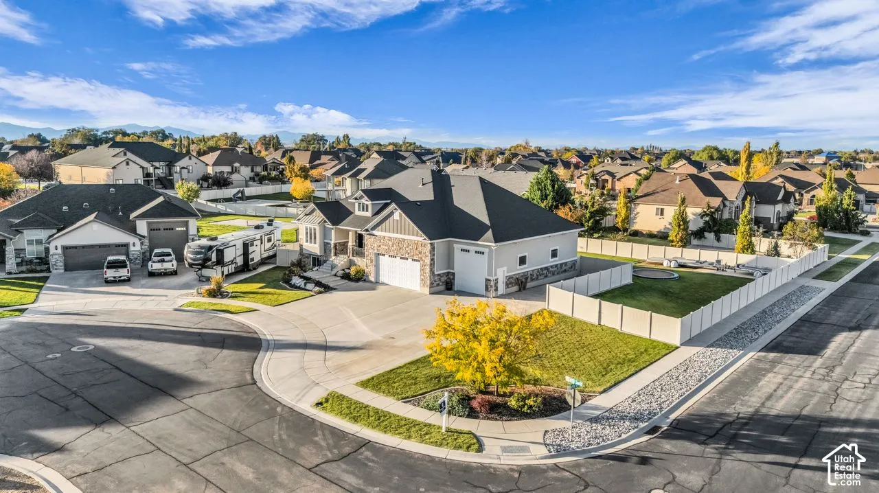 Corner-lot residence featuring a multi-car garage, stone veneer siding, concrete driveway, and white vinyl perimeter fencing