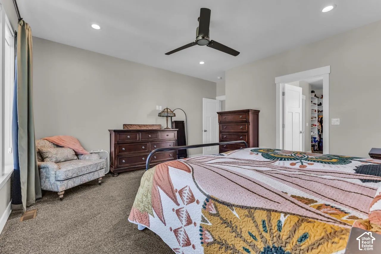 Spacious room featuring neutral wall tones, recessed lighting, carpeted flooring, a dark-finish ceiling fan, and a built-in walk-in closet