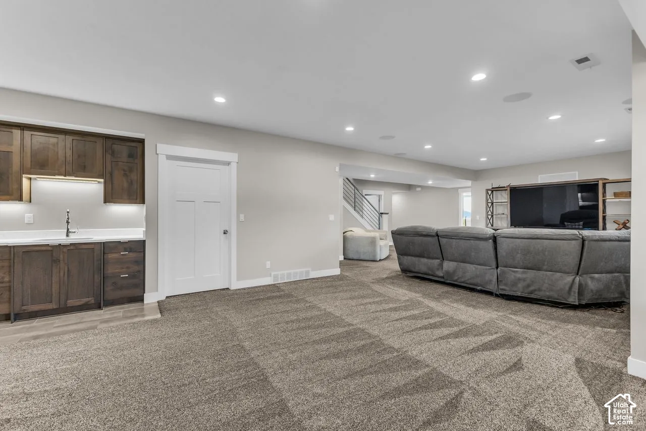 Open-concept space featuring recessed lighting, wet bar with wood cabinetry and quartz countertops, built-in shelving, and carpeted flooring