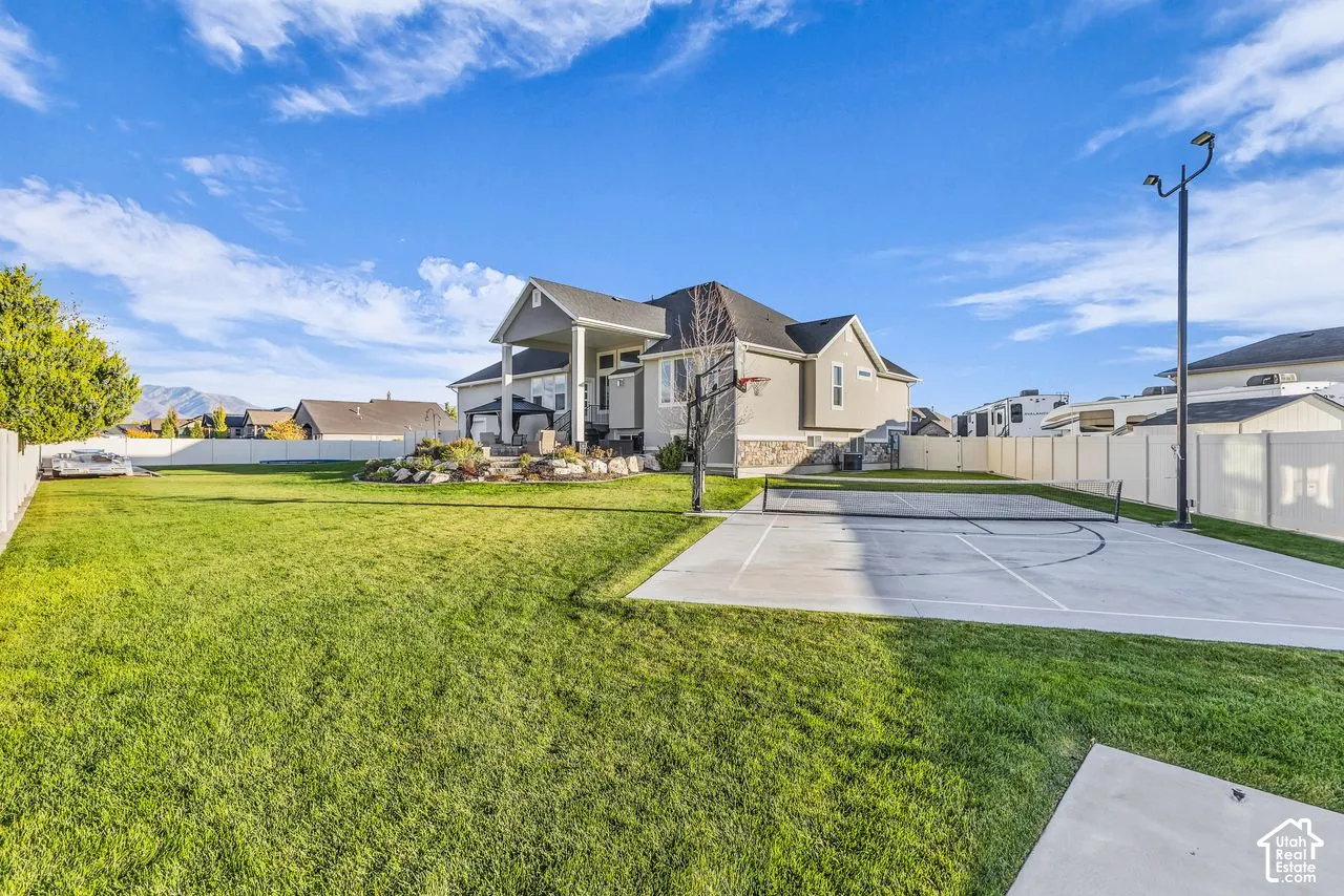 Spacious backyard featuring a manicured lawn, a concrete sport court, built-in basketball hoop, elevated stone landscaping, and full perimeter vinyl fencing