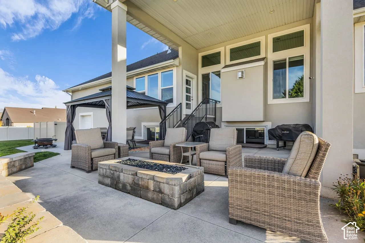Covered concrete patio featuring a built-in stone fire pit, tiered architectural design, and recessed ceiling lighting
