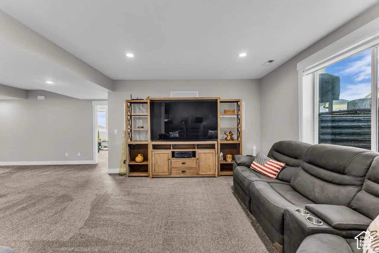 Open-concept interior featuring neutral wall tones, recessed lighting, wall-to-wall carpeting, and a built-in wooden media console with integrated shelving