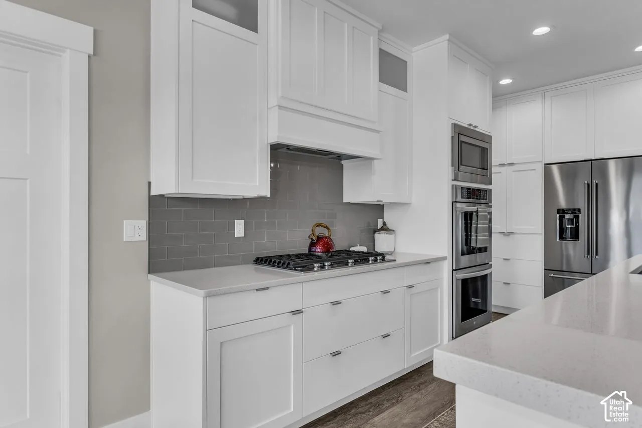 Kitchen featuring white Shaker-style cabinetry, quartz countertops, subway tile backsplash, stainless steel built-in double oven, and wood-finish flooring
