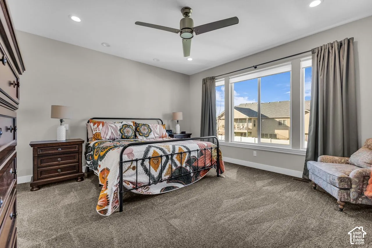 Neutral-toned bedroom featuring carpeting, large multi-pane windows, and a ceiling-mounted light fixture with integrated fan