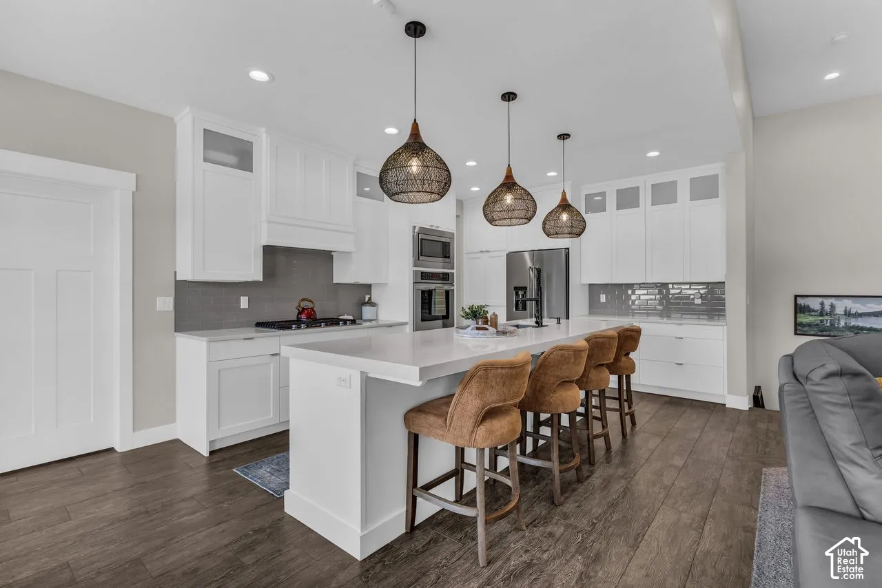 Kitchen featuring white shaker-style cabinetry with glass-front uppers, quartz countertops, a grey subway tile backsplash, stainless steel double wall ovens, and wood-finish flooring
