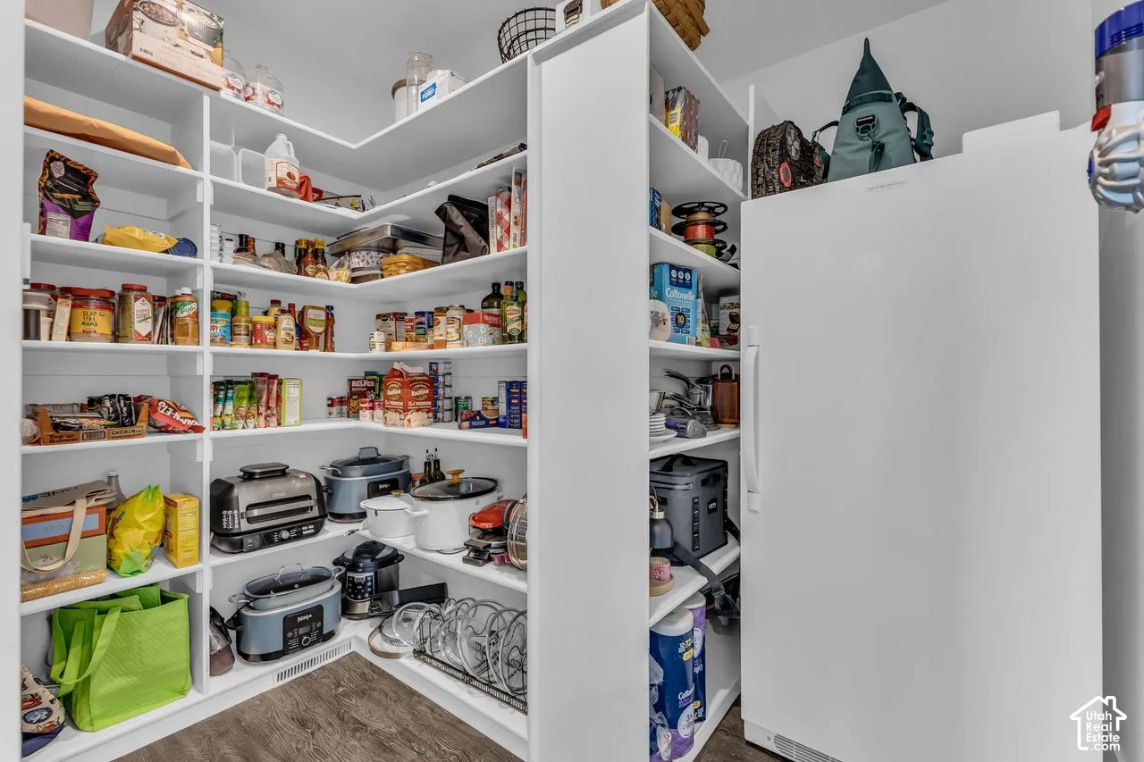 Walk-in pantry featuring white wrap-around shelving, wood-finish flooring, and a dedicated space for a full-size upright freezer