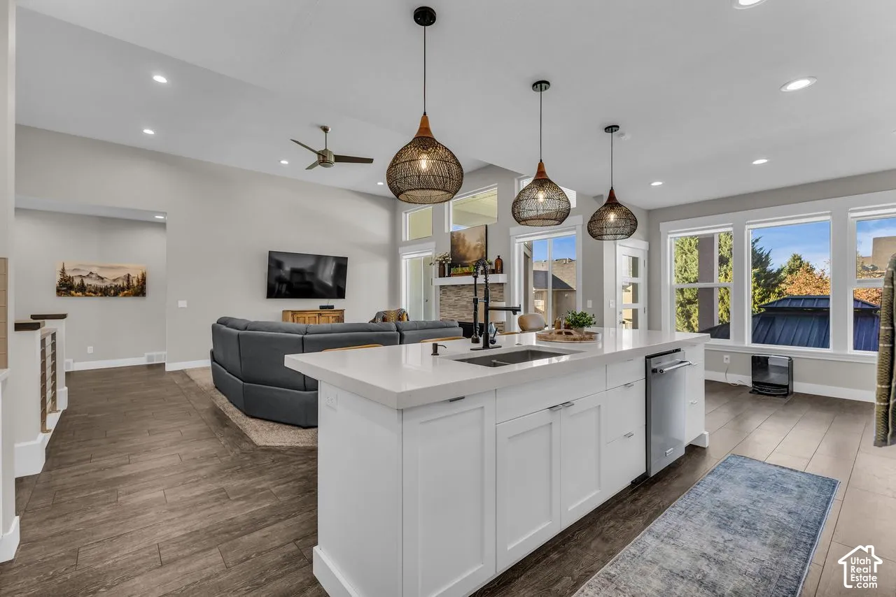 Kitchen featuring a central island with quartz countertops, undermount stainless steel sink, wood-finish flooring, recessed lighting, and three textured pendant lights