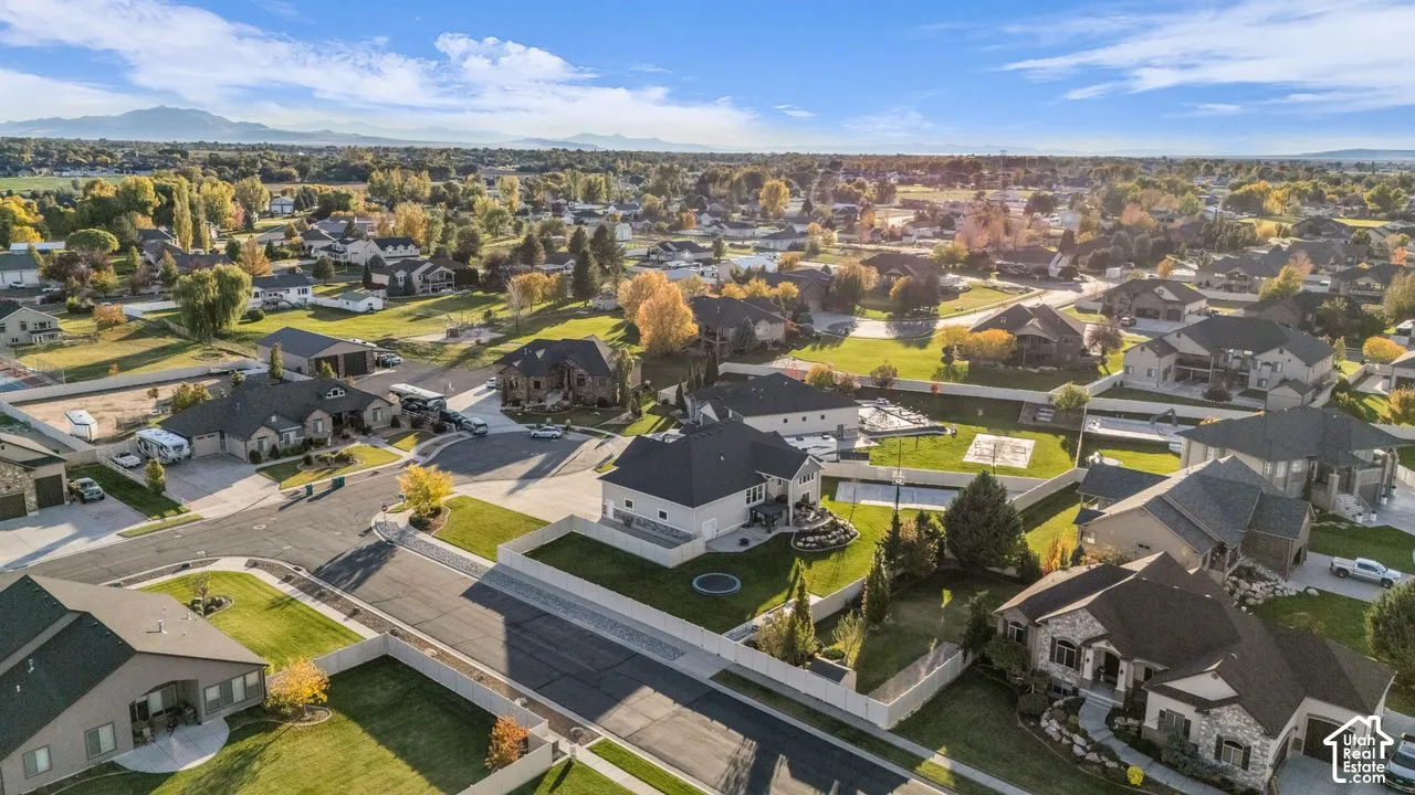 Aerial perspective of a residential neighborhood featuring asphalt paved streets, expansive grass lawns, mature trees, and a mountain range backdrop