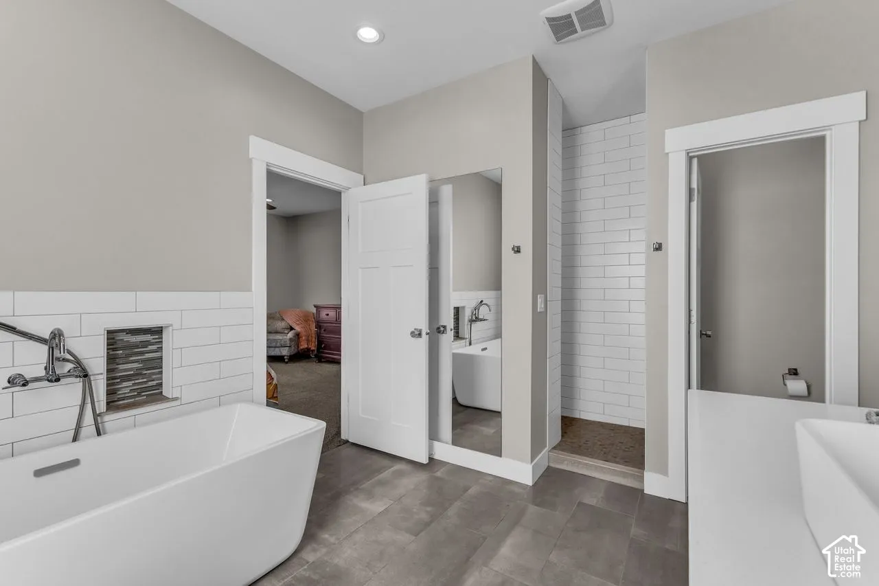 Freestanding soaking tub with wall-mounted faucet, subway tile backsplash, recessed tiled shower niche, large-format floor tile, and solid-surface vanity countertop