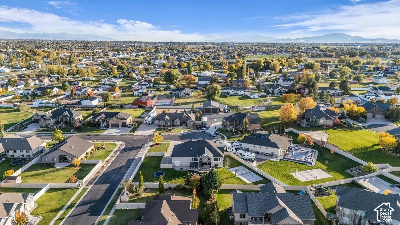 Aerial perspective of the residential neighborhood featuring asphalt-paved streets, established landscaping with mature trees, vinyl fencing, and mountain topography in the distance