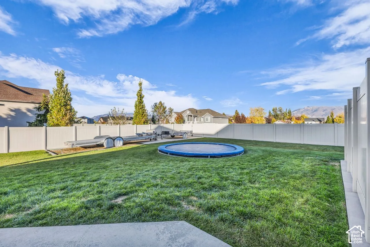 Fully fenced backyard featuring a grass lawn, gravel side area, and concrete patio