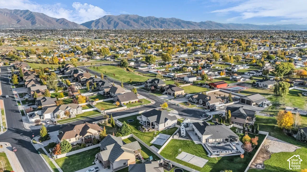 Aerial perspective of a suburban neighborhood featuring paved streets, established residential lots, expansive green spaces, and a mountain range backdrop