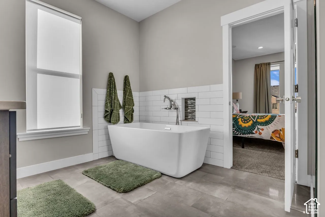 Freestanding soaking tub featuring white subway tile surround, wall-mounted chrome faucet, recessed tiled niche, and large-format tile flooring