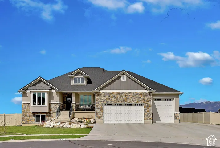 Exterior facade featuring stone veneer detailing, vertical siding, a multi-car garage, and a covered entryway with iron railing