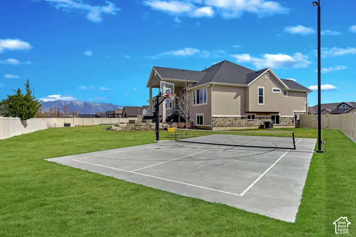 Expansive backyard featuring a concrete sports court with a basketball hoop, manicured lawn, and mountain backdrop