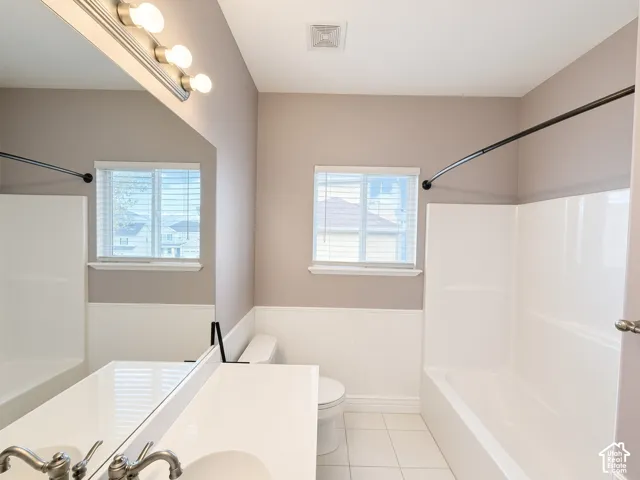 Full bathroom featuring white beadboard wainscoting, an integrated sink with a solid-surface vanity, a large wall-mounted mirror, a tub-shower combination, and tiled flooring