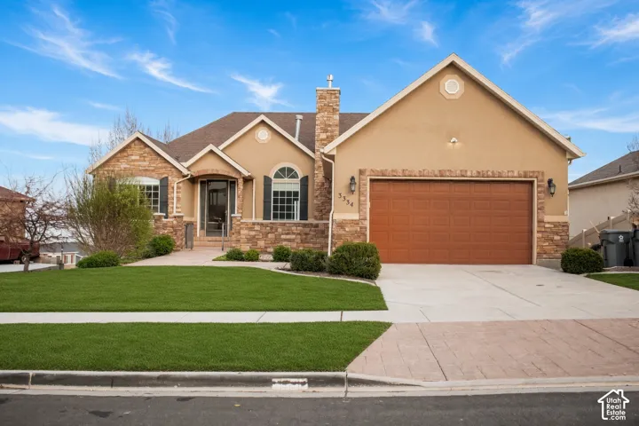 Stucco and stone veneer exterior featuring an attached two-car garage, arched window accents, and a front-facing chimney