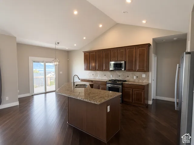 Kitchen featuring a central island with a stone-finish countertop, wood-finish cabinetry, recessed lighting, vaulted ceilings, and wood-finish flooring