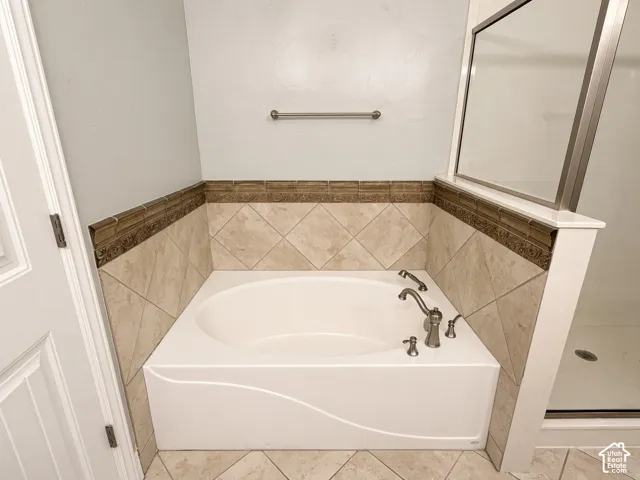 Built-in soaking tub with a curved apron, diamond-patterned tile surround, decorative tile border, and brushed metal faucet fixtures
