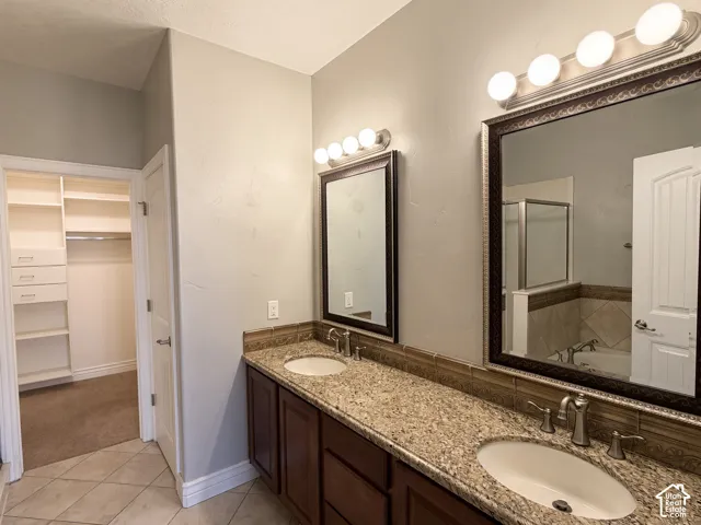 Dual-sink vanity with stone-finish countertop, dark wood cabinetry, two framed mirrors with integrated multi-bulb lighting, and a walk-in storage area featuring custom built-in shelving
