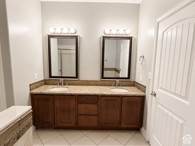 Dual-sink vanity featuring stained wood cabinetry, stone-finish countertops, decorative tile backsplash, framed mirrors, and dual four-light fixtures