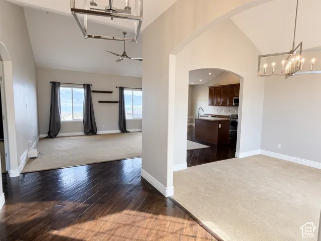 Interior space featuring vaulted ceilings, wood-finish flooring, arched architectural detailing, brushed metal geometric chandeliers, and dark wood cabinetry