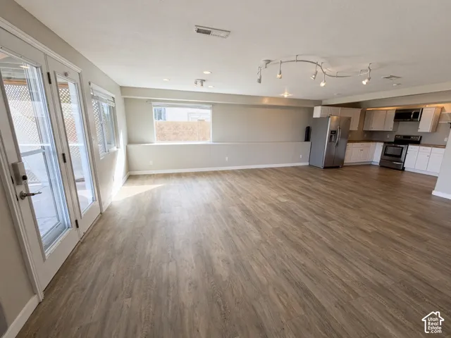 Open-concept interior featuring wood-finish flooring, glass-paned double doors, recessed and track lighting, and a kitchen equipped with white cabinetry and stainless steel appliances
