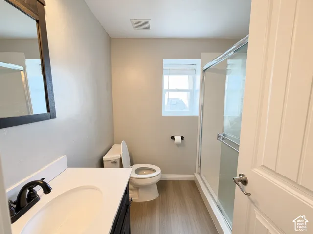 Bathroom featuring a dark wood-finish vanity with a white countertop and oval under-mount sink, matte black faucet, and a glass-enclosed shower with wood-finish flooring