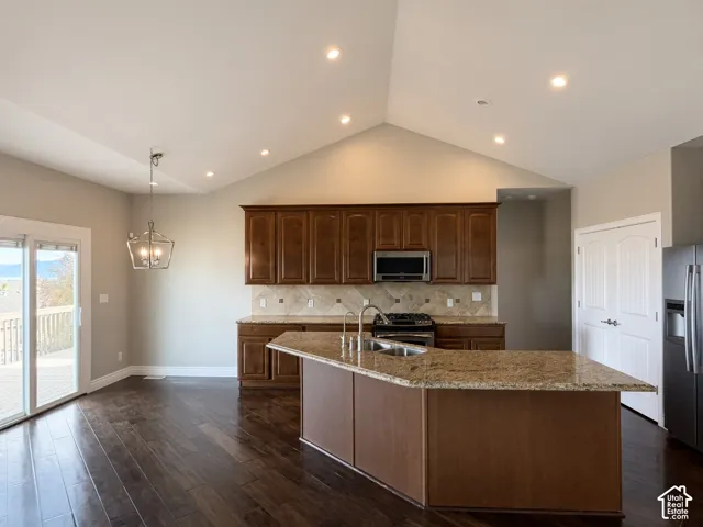 Kitchen featuring a vaulted ceiling, wood-finish cabinetry, stone-surface countertops, wood-finish flooring, and a stone tile backsplash